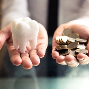 Hands holding coins and tooth demonstrate cost of dental implants in Naples
