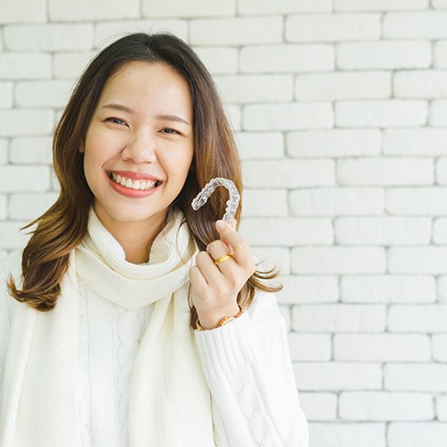 Woman smiling while holding Invisalign aligner