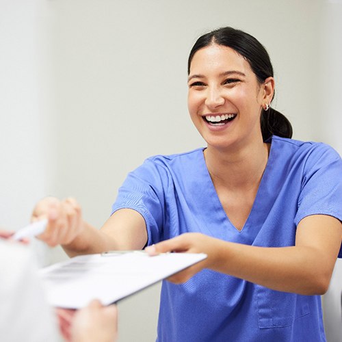 Dental assistant smiling while handing patient form