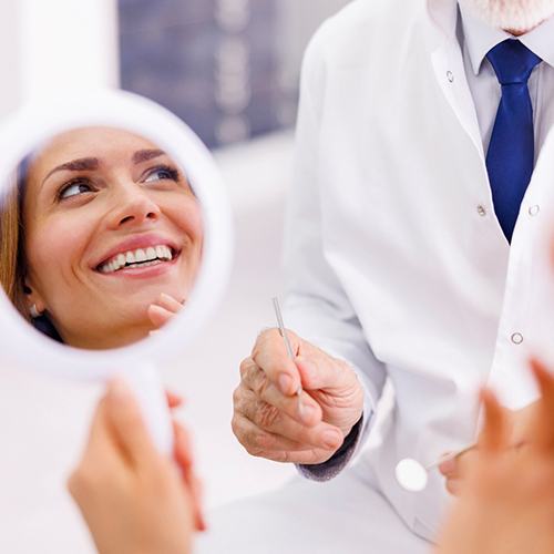 Patient smiling at dentist while holding handheld mirror